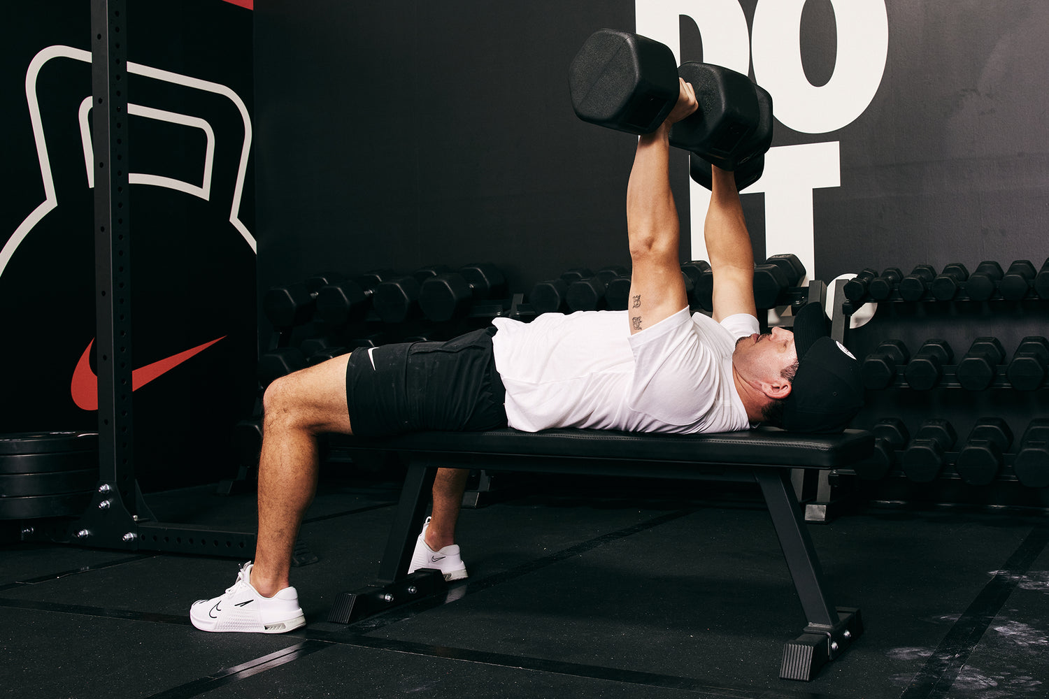 Male Athlete lying on the Nike Flat Weight Bench and bench pressing Nike Dumbbells