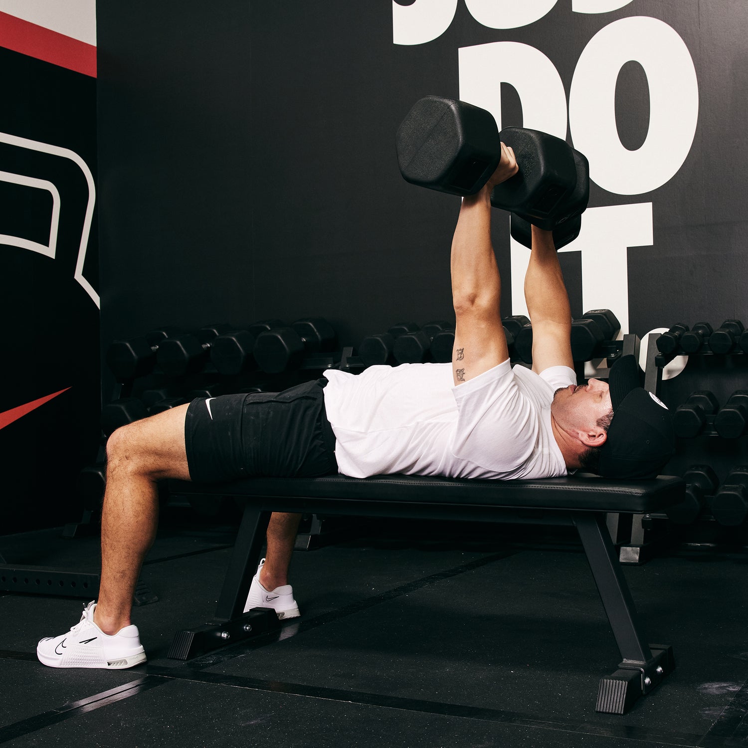Male Athlete lying on the Nike Flat Weight Bench and bench pressing Nike Dumbbells