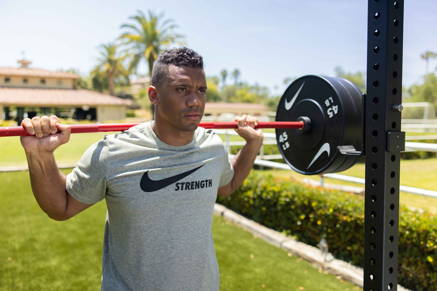 Nike athlete Russell Wilson squatting outdoors with the Nike Coated Premium Barbell 20kg red swoosh 
