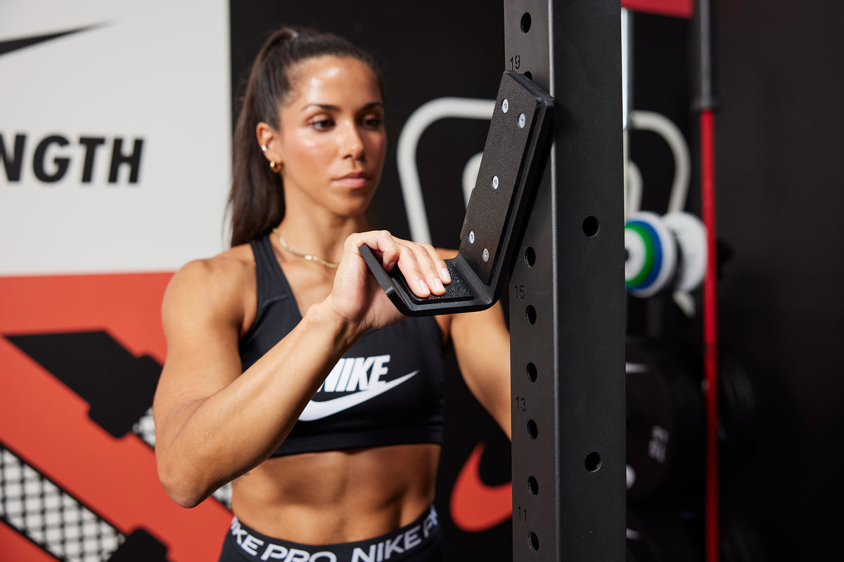 Female athlete attaching the J-cup to the Nike Squat Cage