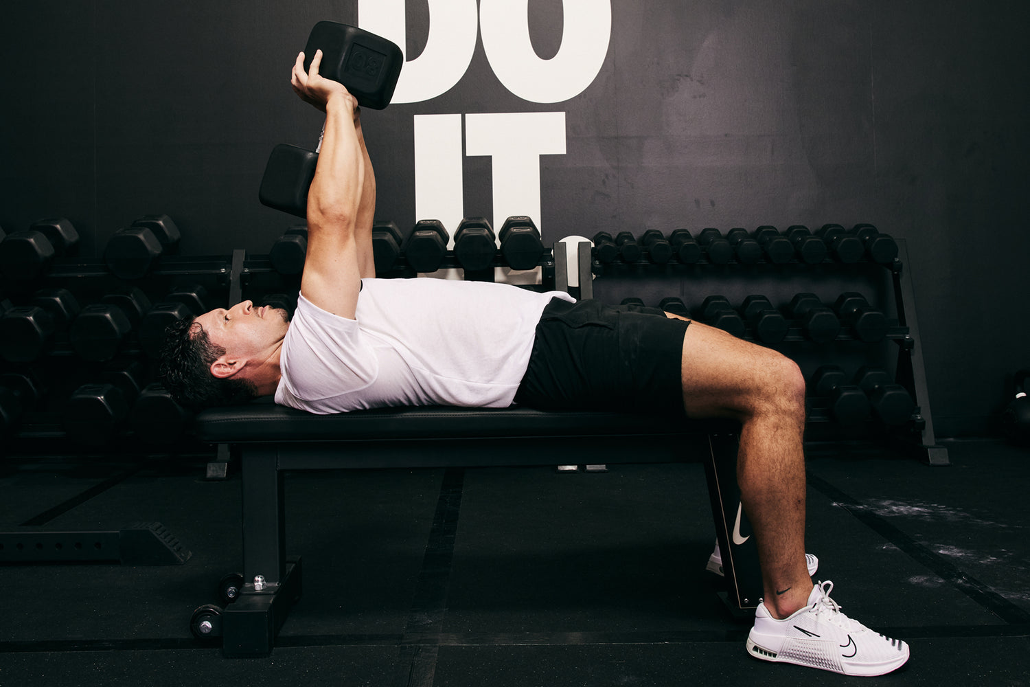 Male athlete lying on the Nike Rolling Weight Bench doing a tricep press with Nike Dumbbell