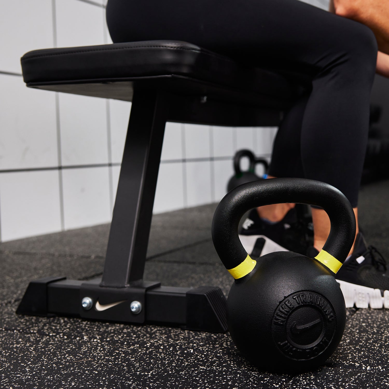 Female athlete sitting on the Nike Flat Weight Bench next to two Nike Kettlebells 35 LB