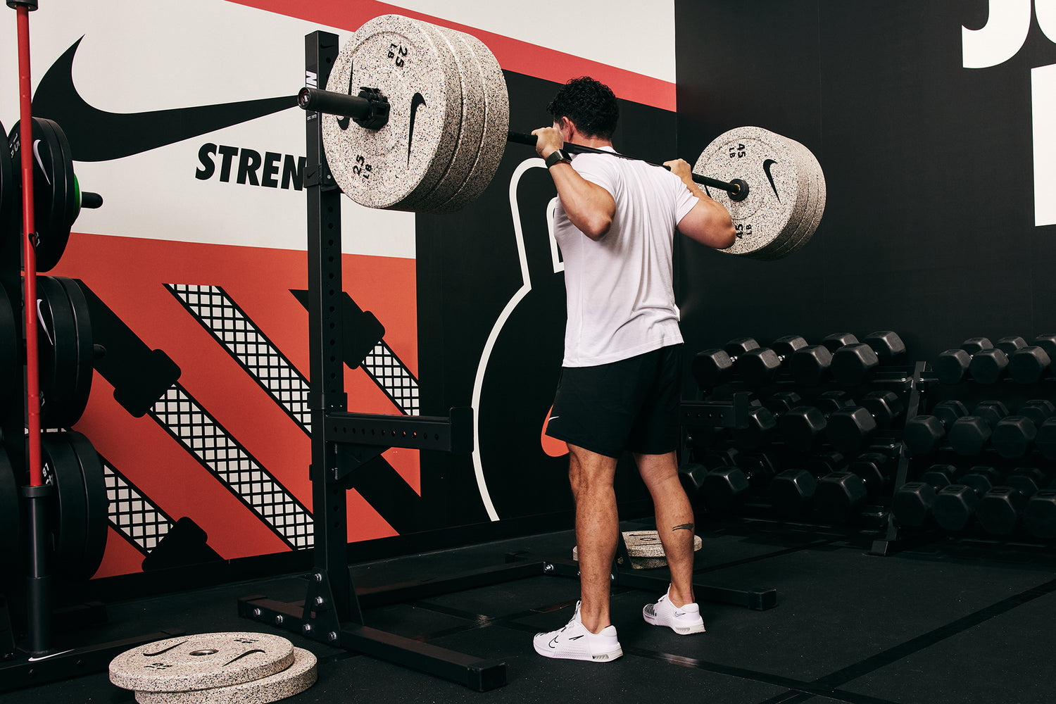 Male athlete squatting heavy with the Nike Barbell 20kg Black Chrome, Nike Rubber Bumper Plate (Grind), and the Nike Squat Stand