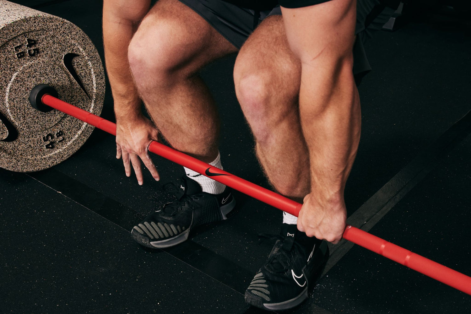 Male athlete preparing for a deadlift with the Nike Coated Premium Barbell 20kg red swoosh with medium knurl